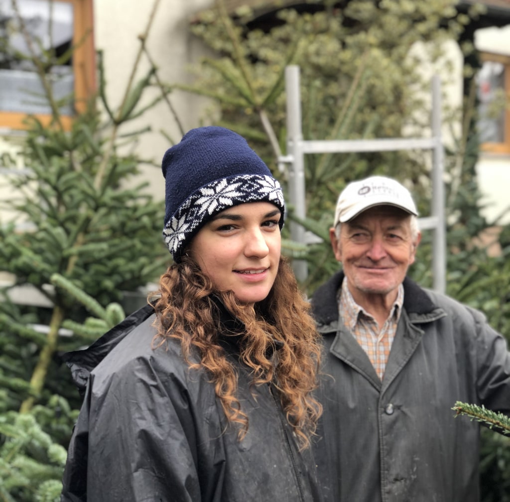 Junge Frau und Opa vor Christbäume